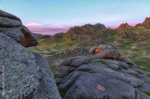 Huge stone boulders with round edges and lush greenery and wood. Pointed mountains rocks. Summer autumn landscape at sunset or sunrise