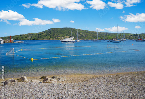 Fototapeta Naklejka Na Ścianę i Meble -  A tranquil coastal scene featuring clear turquoise waters, anchored yachts, and a green hillside under a bright blue sky in Primosten, Croatia.
