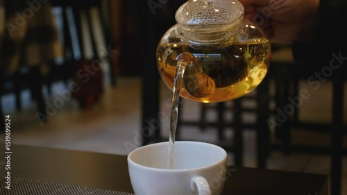 Pouring tea from a glass teapot into a white cup