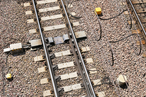 Railway track switch mechanism. Metal rails and gravel with signal cables. Railroad infrastructure detail. Train track junction equipment. Transport engineering and railway maintenance system.