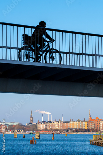Urban waterfront cyclist on bridge with city skyline and clear weather, perfect for themes of freedom, clean commuting and metropolitan life.