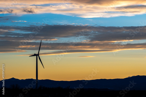 Wind turbine silhouette at dusk with vibrant sky colors and horizon in Zaragoza, Spain, suitable for sustainability visuals with copy space available.