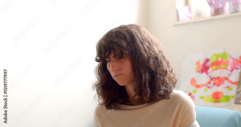 A woman with beautiful, curly hair is sitting in a cozy and inviting indoor atmosphere, lost in her thoughts, while colorful and vibrant artwork decorates the background space A woman with beautiful, curly hair is sitting in a cozy and inviting indoor atmosphere, lost in her thoughts, while colorful and vibrant artwork decorates the background space