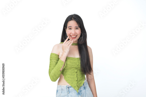 Young Southeast Asian woman in trendy green ruched top giggling playfully with her hand near her mouth, suggesting mischief. Isolated on a light background.