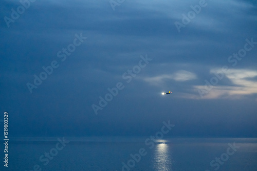 A plane coming in for landing at night, flying over the sea