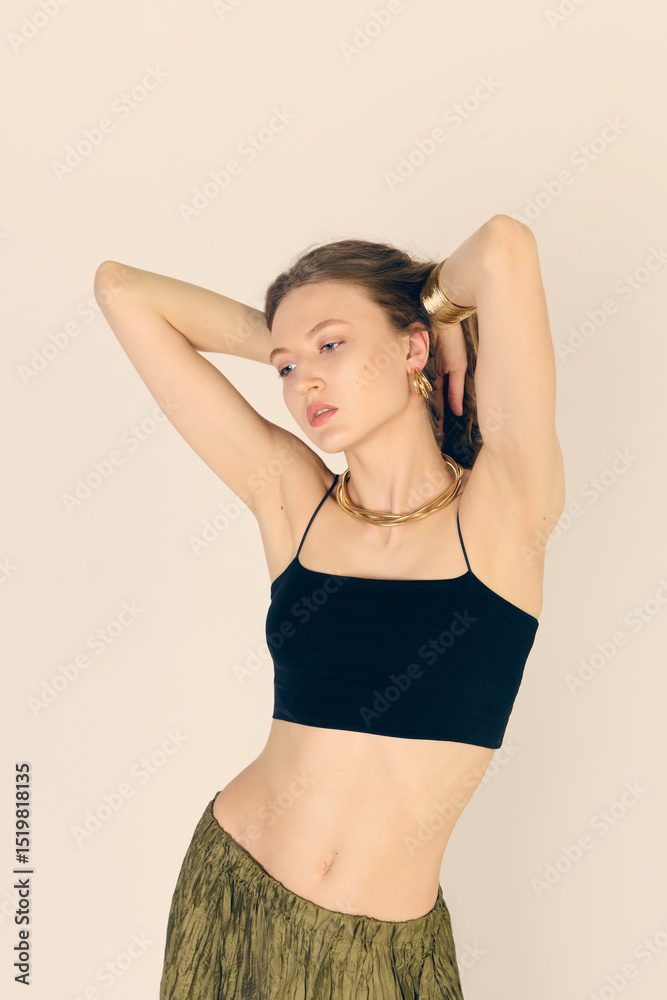 Obraz premium Curly-haired elegant woman in gold jewelry poses on a light background