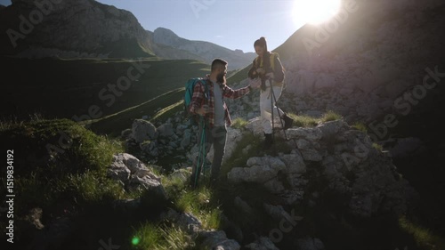 Young tourist couple hiking up scenic mountain trail during golden sunrise, experiencing breathtaking wilderness landscape with energetic and passionate exploration