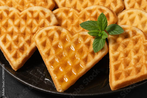 Delicious heart-shaped waffles with syrup and mint on a black plate, perfect for breakfast or dessert