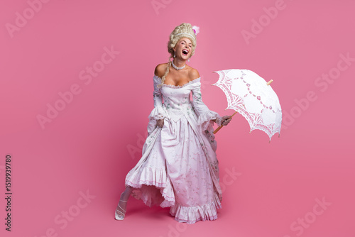 Elegant young woman dressed in vintage baroque costume with corset and parasol on pink background