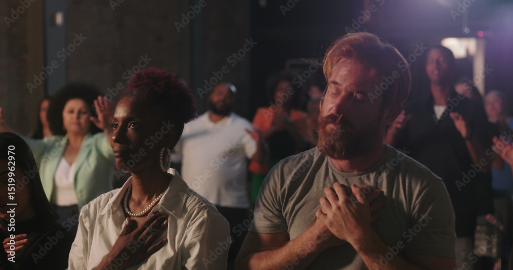 Obraz premium Man with hands on chest in deep prayer during spiritual gathering, surrounded by diverse congregation, African American woman praying beside him, faith and devotion emphasized