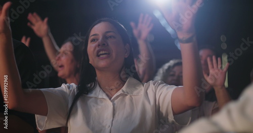 Woman raising hands in spiritual praise during evangelical worship service, joyful expression, white shirt, diverse congregation with hands lifted in celebration of faith