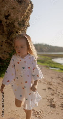 Happy little child girl running on sandy beach with sunset sunlight