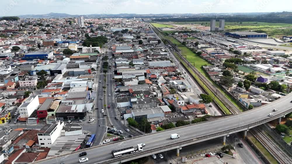 Vista aérea panorâmica de Mogi das Cruzes com áreas residenciais, prédios e vegetação ao fundo. Cidade em desenvolvimento com áreas urbanas e verdes