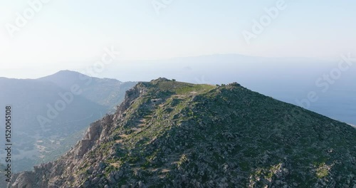Aerial view over a green mountain peak, opening to a cinematic view of a valley on a Mediterranean island.