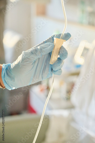 Hand wearing a blue nitrile glove adjusts the intravenous drip used to administer fluids and medications to a hospital patient.