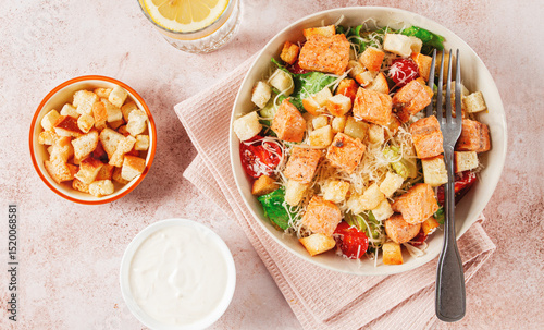 caesar salad with salmon, with croutons and dressing, in a salad bowl, on a pink table,