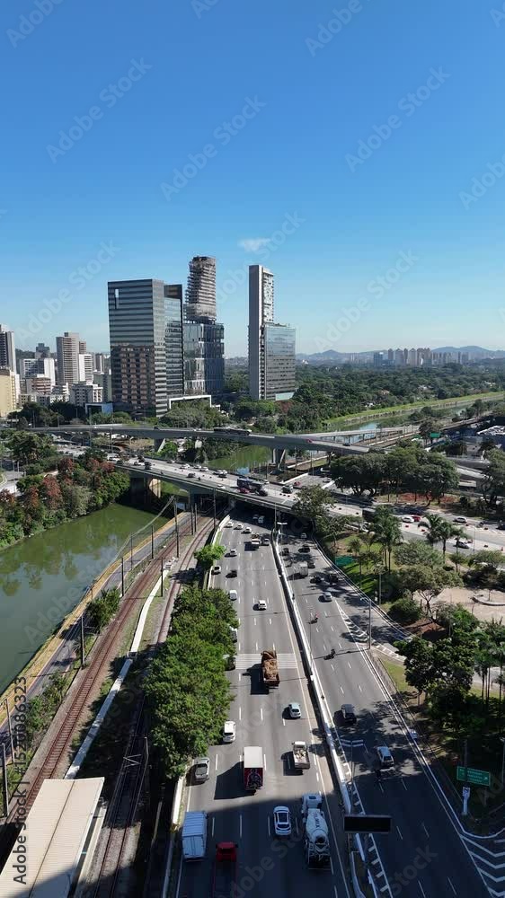 Visão aérea vertical da movimentada Rodovia Marginal Pinheiros em São Paulo, SP, mostrando o fluxo intenso de veículos e a dinâmica urbana da cidade, com destaque para a infraestrutura