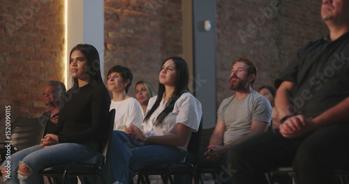 Group of people sitting in front of a cross in a spiritual setting, with a woman in focus looking upward, others in a meditative pose