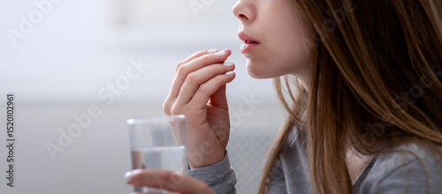 Tableau sur toile Side view of young woman with glass of water taking sleeping pill or antidepressant, copy space