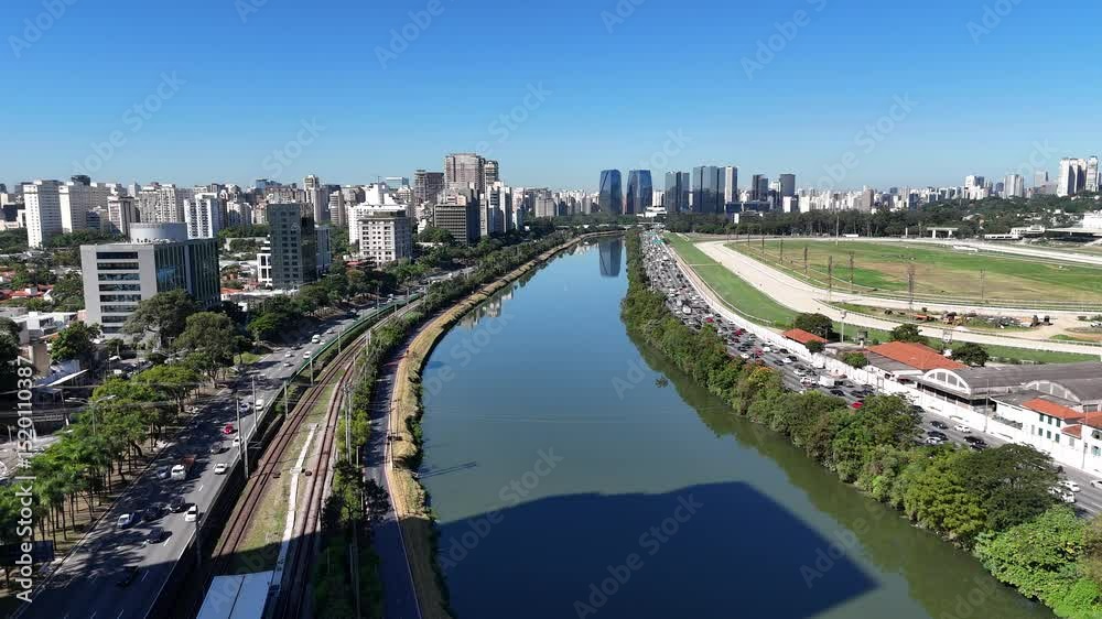 Visão aérea feita por drone da Marginal Pinheiros com bastante trânsito. A imagem mostra longas filas de veículos ao lado do rio, refletindo a rotina intensa da cidade de São Paulo