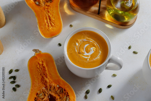 Roasted butternut squash soup with cream and pumpkin seeds on two white mugs.