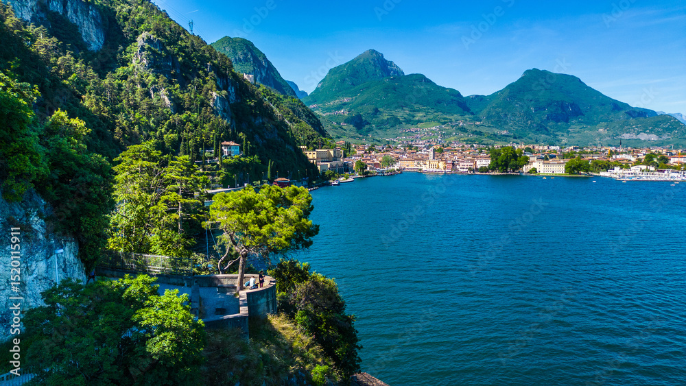Obraz premium Aerial view of Riva del Garda with Torre Apponale, MAG museum, bike paths, boats and river ferries connecting towns, surrounded by mountains and clear Lake Garda water, full of tourists