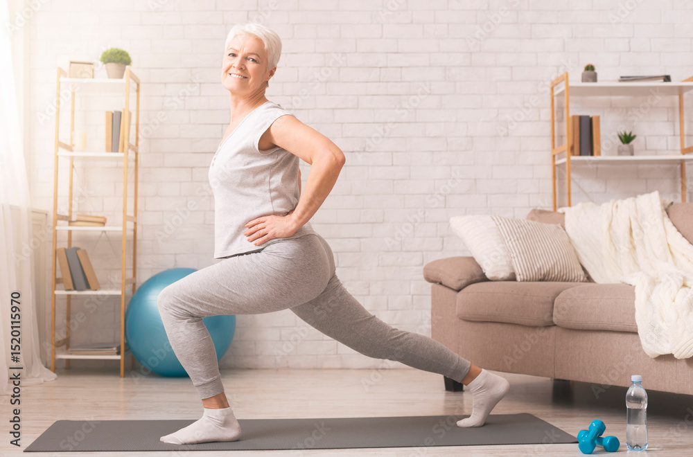 Fototapeta premium Legs stretching. Sporty senior lady doing lunges at home, empty space