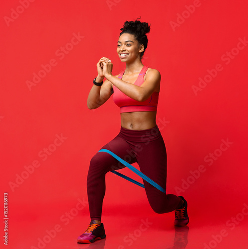 Photos Cheerful black fitness girl making working out with resistance band over red stu