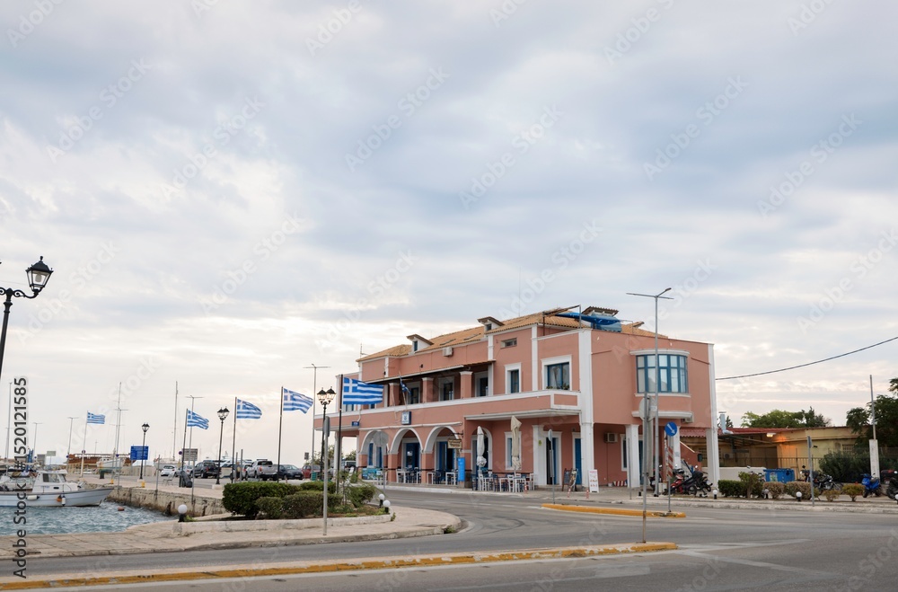 Obraz premium Fair weather enhances the vibrant atmosphere as tourists gather at a friendly waterfront cafe in Zakynthos, Greece. Flags flutter while laughter fills the air, embodying summer joy
