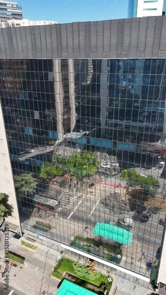 Imagem aérea vertical mostra reflexo da cidade em prédio espelhado enquanto carros passam em tráfego intenso