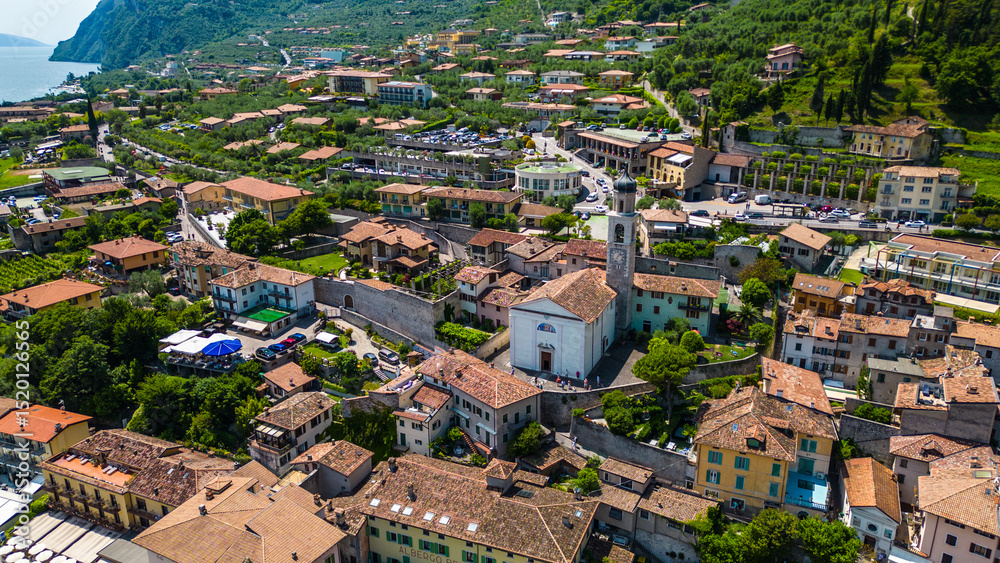 Obraz premium Aerial view of Limone sul Garda, a charming lakeside town with colorful houses, lush lemon terraces, bike paths along Lake Garda, and majestic mountains surrounding the crystal-clear water