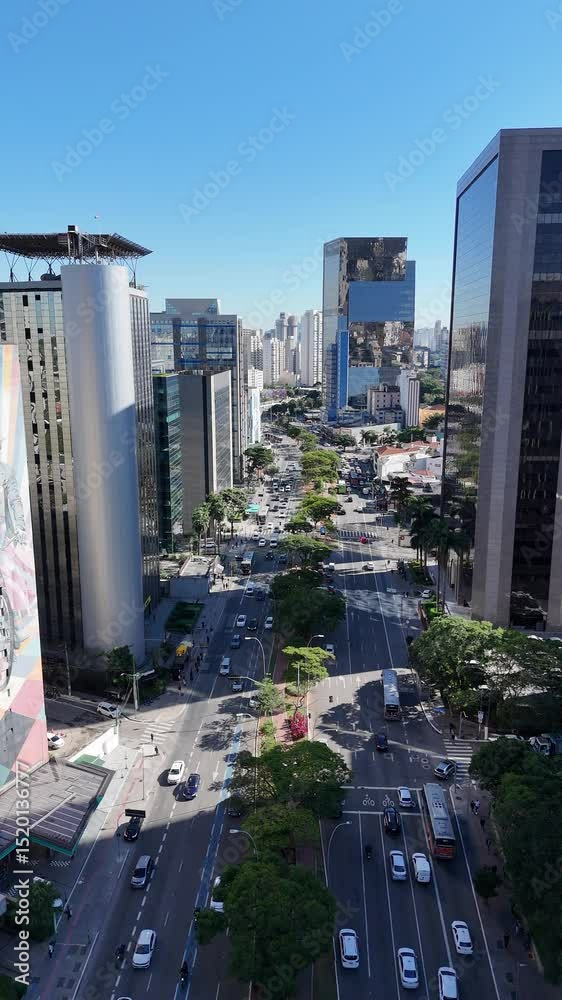 Visão aérea do trânsito de veículos entre os prédios da Avenida Faria Lima, em São Paulo. A imagem destaca o contraste entre o fluxo urbano e a arquitetura moderna da capital paulista
