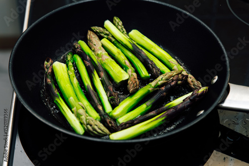 Fresh asparagus cooking in a skillet on a stovetop in a modern kitchen