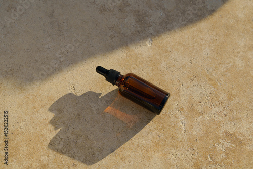 Brown glass mockup of serum jar with pipette dispenser for face on travertine lit by the sun near the sea. Concept of cosmetics, beauty products, aesthetics, skin care.