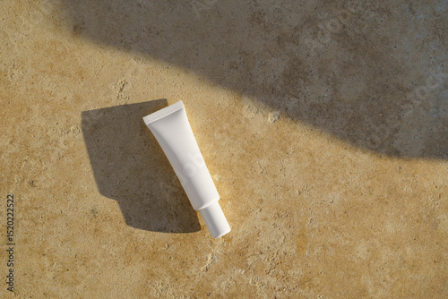 White thin mockup tube of face or eye cream on travertine illuminated by the sun. Concept of natural skin care products, its nutrition, hydration and protection.