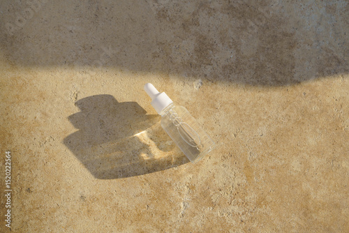 Transparent glass mockup jar with a pipette of serum for face on travertine lit by the setting sun near the sea. Concept of natural cosmetics, beauty products, skin care. Image for your design