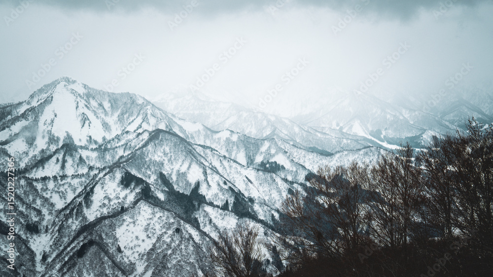 Obraz premium Skiers enjoy the slopes of Gala Yuzawa with stunning views of Ishiuchi Maruyama and Yuzawa Kogen in Niigata, Japan. Snow-covered mountains and a small town stretch across a scenic winter valley.