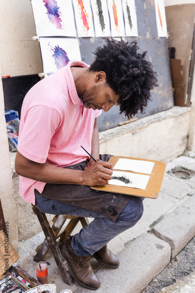 Fototapeta premium African American artist or painter with dreadlocks and afro hair painting on the street in Latin America, street art drawing of an Afro-Caribbean man