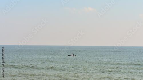 Lone fisherman on a small boat in calm sea under a clear sky at Bay of Bengal.