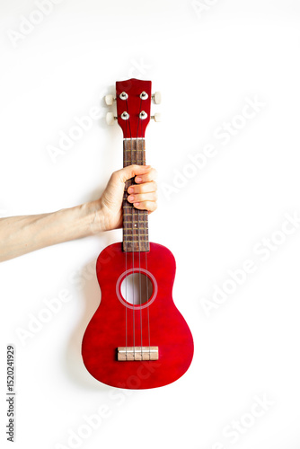 Hand is holding red small guitar ukulele. Musical instrument