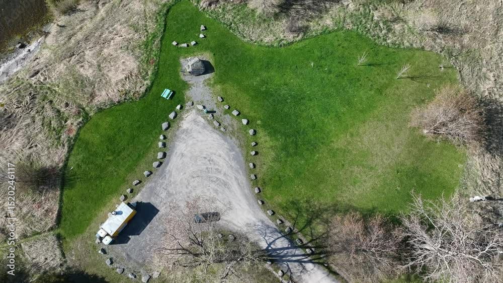 triangular gravel parking area with a yellow van, surrounded by green grass and scattered boulders
