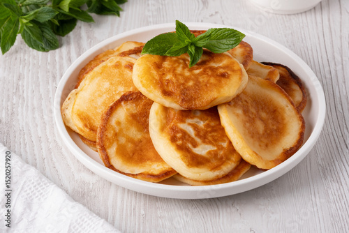 Delicious golden pancakes served with fresh mint leaves on a white plate in a cozy kitchen