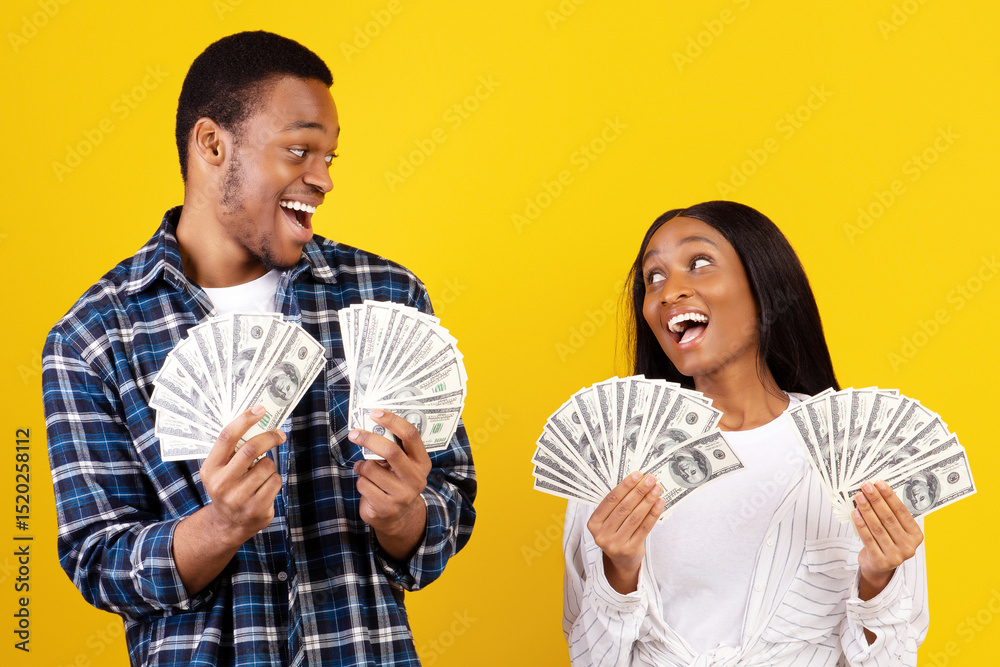 A lot of money and win. Millennial african american male and female hold many dollars in hands and expressing success at covid-19 quarantine, isolation on yellow background, studio shot, copy space A lot of money and win. Millennial african american male and female hold many dollars in hands and expressing success at covid-19 quarantine, isolation on yellow background, studio shot, copy space