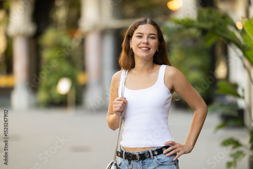 фотографія Carefree attractive young woman in mid twenties with fair skin and long hair walking outside on warm sunny summer day, dressed in casual jeans and white top