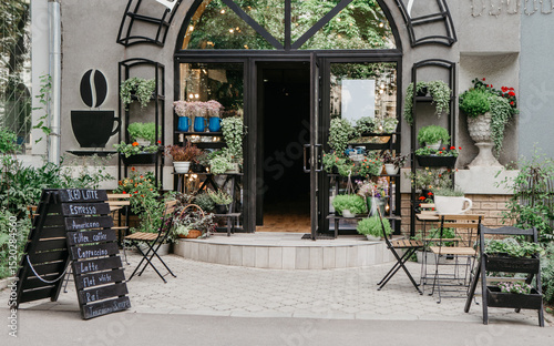 Fototapeta Naklejka Na Ścianę i Meble -  Eco cafe on street and flower studio, small business in city, reopening after covid-19, outdoor interior. Sign board with menu, tables for clients, potted plants on shelf at modern store, nobody