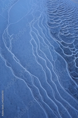 Close-up of textured ice surface with natural patterns including curved lines and scale-like formations in cool blue tones evoking calm and cold atmosphere