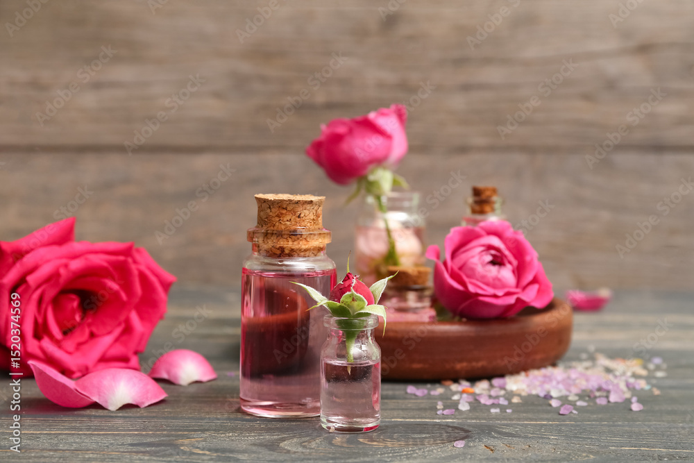 Bottles of cosmetic oil with rose extract and flowers on wooden table Bottles of cosmetic oil with rose extract and flowers on wooden table