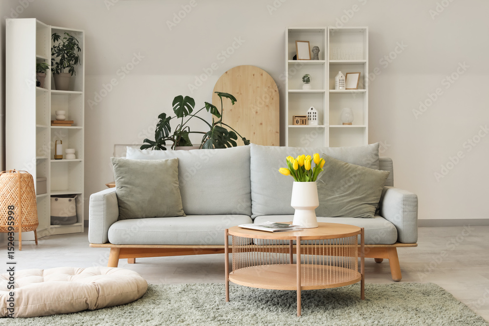 Obraz premium Modern interior of light living room with cozy sofa and coffee table with tulips