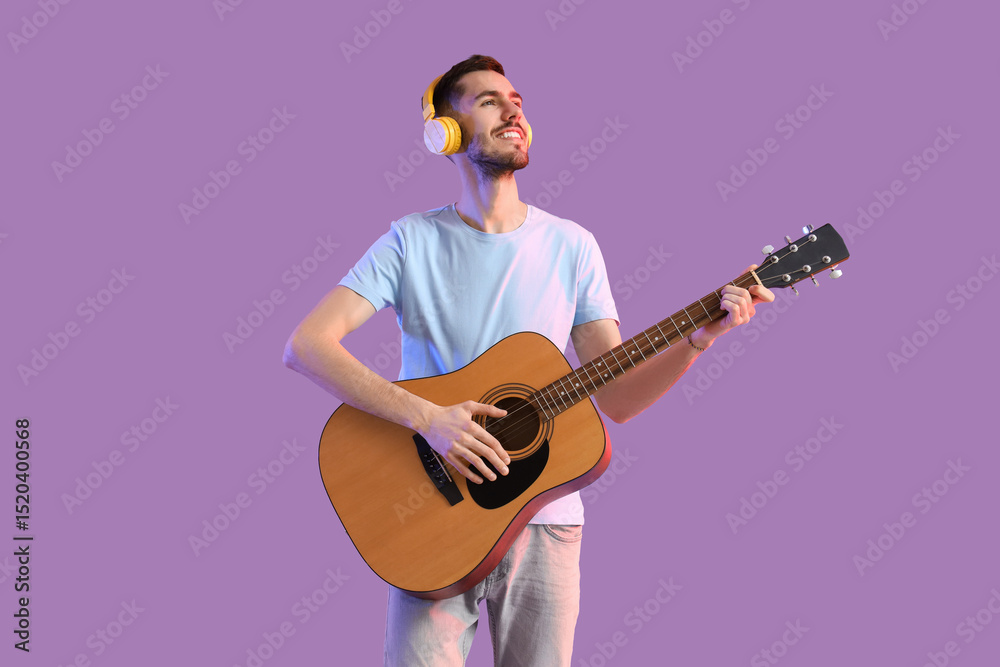 Obraz premium Young bearded man in headphones playing guitar on lilac background