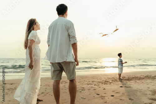 Mom and Dad watch their kids happily fly kites on the beach during a holiday, travel, long weekend, summer or any other holiday. They are happy to spend time together.